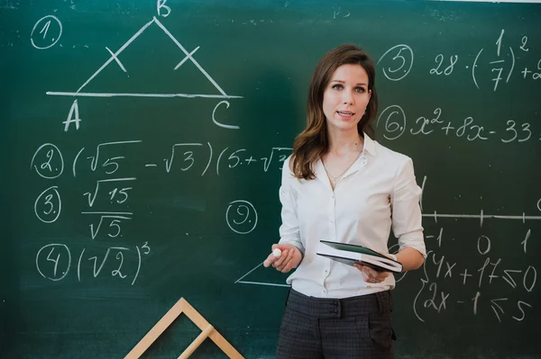 Young attractive female teacher of maths interacting with her young primary school students asking a young girl for an answer