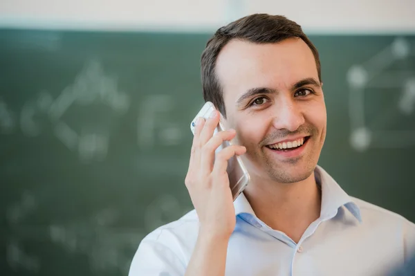 Portrait closeup on a man talking phone at classroom in front of chalkboard