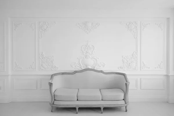 Living room with antique stylish light sofa on luxury white wall design bas-relief stucco mouldings roccoco elements. Black and white photo.