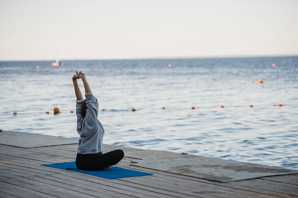 Morning shot of a girl in lotus position doing stretching yoga exercises on the pier