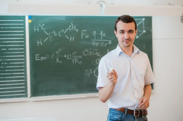 Young teacher near chalkboard in school classroom talking to class