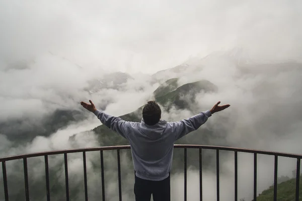 Young traveler man wearing hoodie stands on the viewpoint in national park and watching outstanding foggy landscape. Beautiful moment miracle of nature