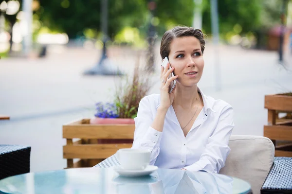 Portrait of young business woman sitting relaxed at outdoor cafe drinking coffee and talking using her cell phone