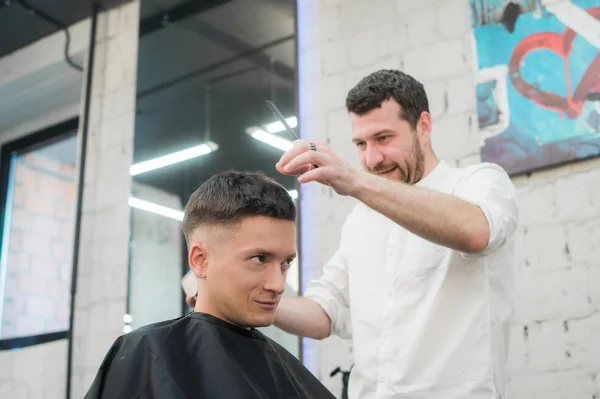 Professional styling. Close up side view of young satisfied man getting haircut by hairdresser with electric razor at barbershop