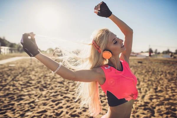 Portrait of young beautiful woman listening to music at beach. Close up face of smiling blonde woman with earphone looking at camera. Girl running at beach and listening to music.