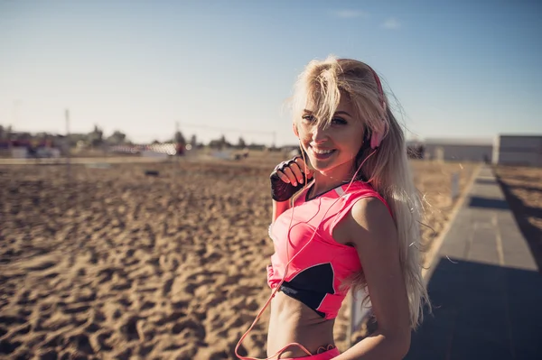 Portrait of young beautiful woman listening to music at beach. Close up face of smiling blonde woman with earphone looking at camera. Girl running at beach and listening to music.