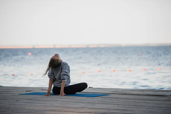 Morning shot of a girl in lotus position doing stretching yoga exercises on the pier