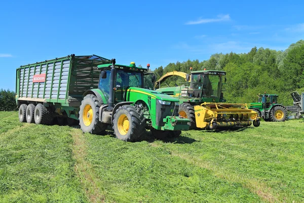 The wheel John Deere 8335R tractor with the trailer and the fodder harvesting John Deere 7450 combine