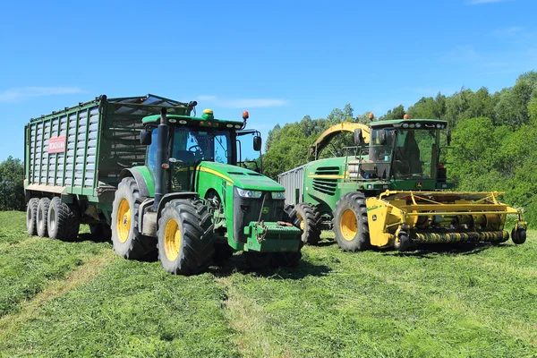 The wheel John Deere 8335R tractor with the trailer and the fodder harvesting John Deere 7450 combine