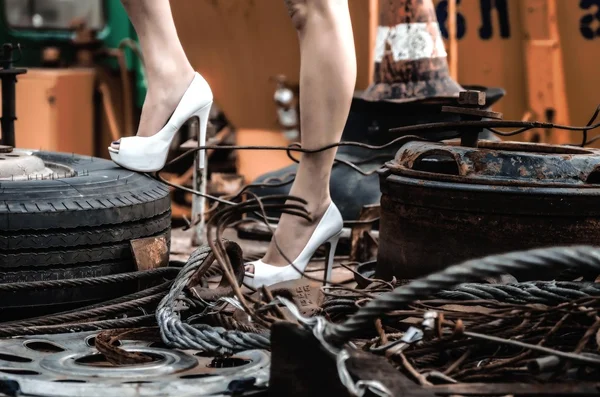 Legs of stylish girl among old tires, spares and wires