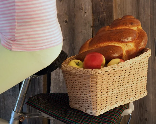 Basket by bicycle with apples and a roll