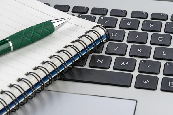 Notebook and pen on the laptop keyboard, close up