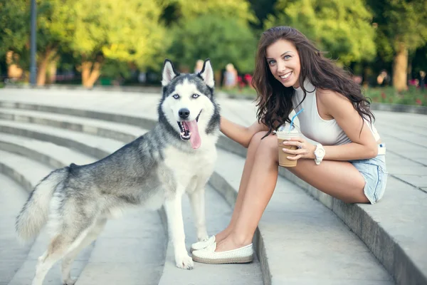 Girl drinking ice coffee and playing with her husky dog in the park