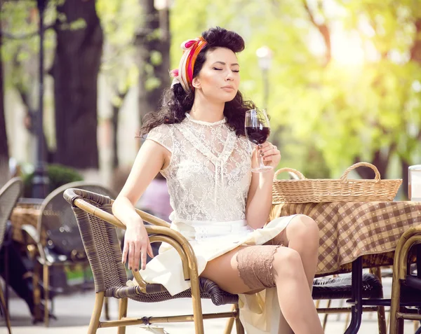Beautiful young girl with glass of red wine alone in a street cafe