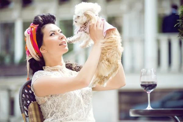 Young Italian woman with little puppy, drinking red wine in an outdoor cafe