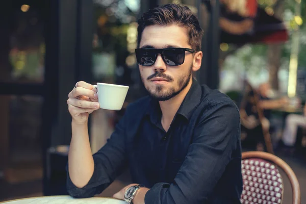 Cutie man with cup of coffee looking at mobile phone outdoors