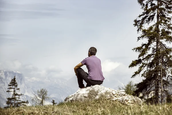 Hiker sitting on rock on a mountain top in alpine landscape