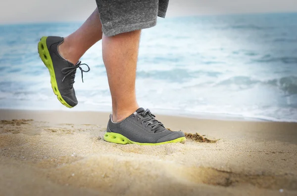Mens feet in sneakers go on the beach.