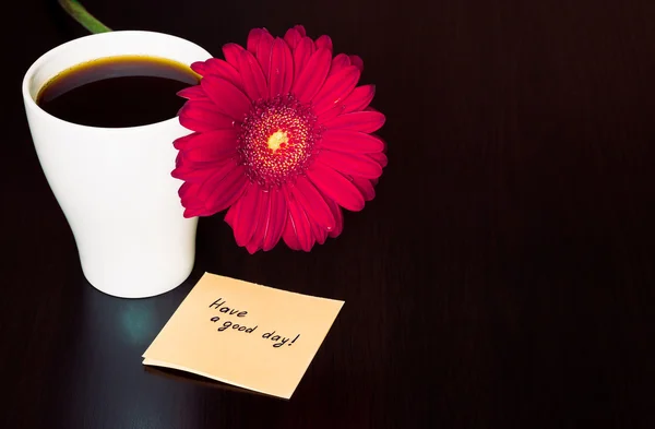 Pink gerbera flower, cup of coffee and paper with text \'\'Have a