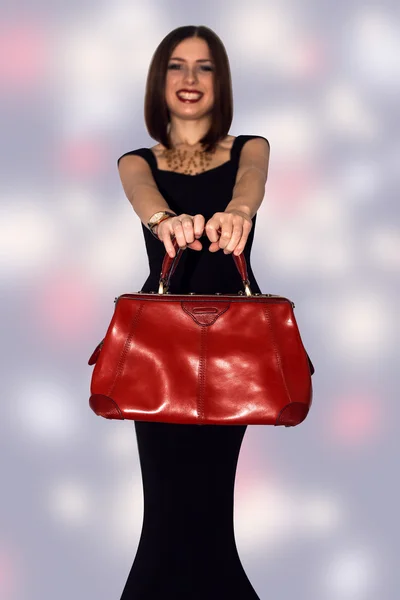 Fashionable sexy woman posing in elegant black dress with red leather handbag in hands