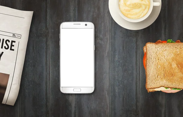 Smart phone with isolated display for mockup on table. Newspapers, coffee and sandwich on table. Top view.