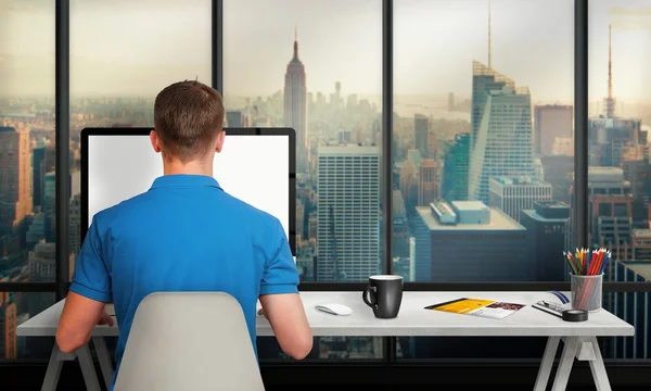 Man working on computer with isolated screen in office interior overlooking the city and skyscrapers. Work desk with keyboard, mouse, cup of coffee, paper, pencils.