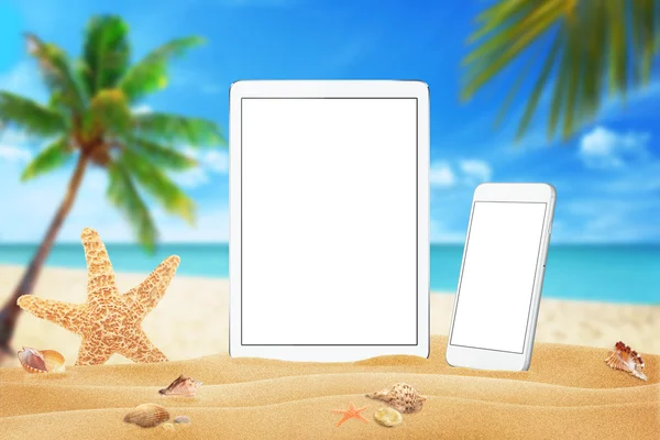 White tablet and smart phone with isolated white screen for mockup. Summer on beach, sea, sand, blue sky, palm, starfish and shells.