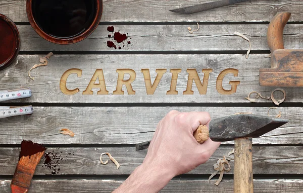 Carving word carved in wood with hammer and chisel. Beside is brush, paint, wood plane, ruler, shavings.