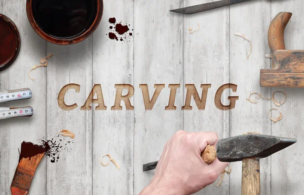 Carving word carved in wood with hammer and chisel. Beside is brush, paint, wood plane, ruler, shavings.