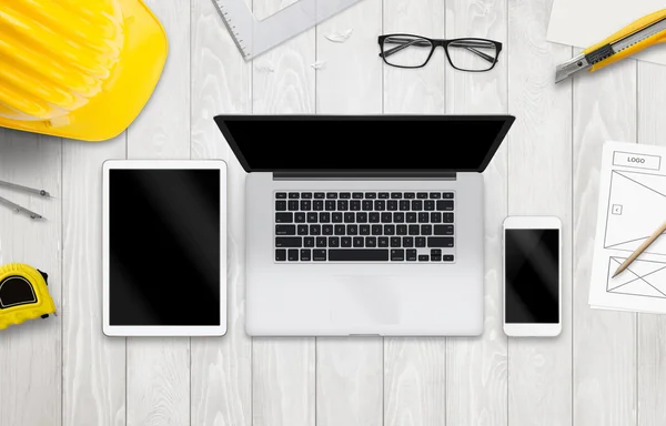 Laptop computer, tablet and smart phone mockup. Work desk with glasses, paper, pencil, construction tools.