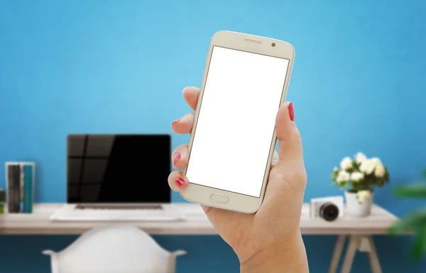 Smart phone with isolated screen for mockup in office interior. Computer and blue wall in background.