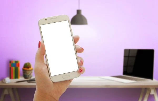 Smart phone with isolated screen for mockup in woman hand. Office interior with computer and pink wall in background.