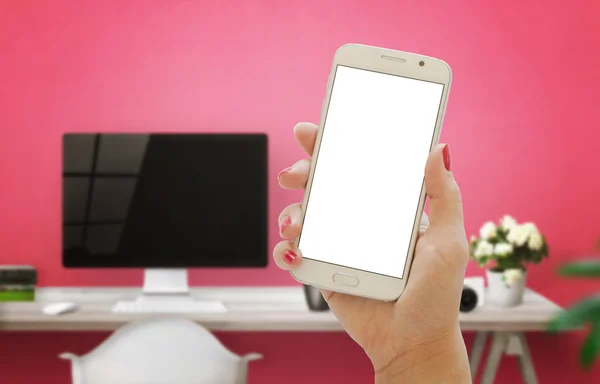 White smart phone in woman hand. Female mockup in office interior with computer and pink wall in background.