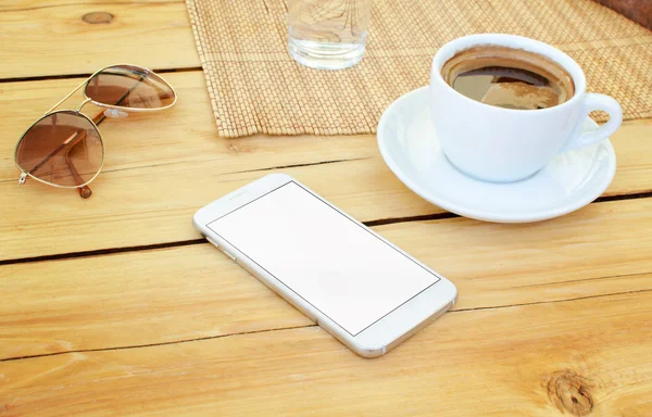 Smart phone placed on table. Isolated screen for mock-up. Coffee and glasses beside.