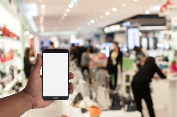 Hand of man hold mobile phone over blurred image of people shopping in department store