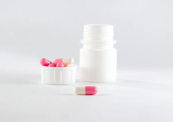 White-Pink pills spilling from a white plastic bottle
