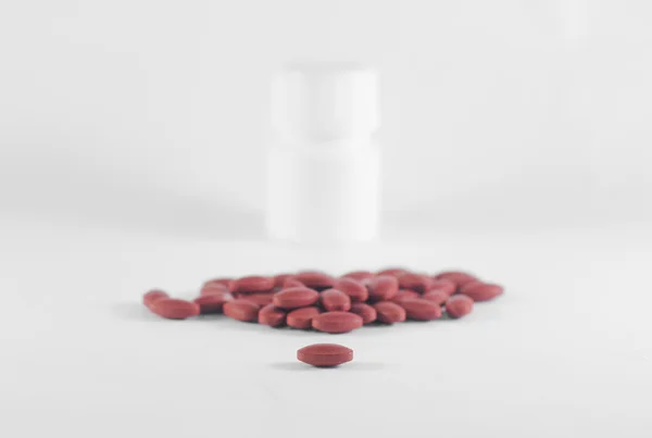 Dark red pills spilling from a white plastic bottle