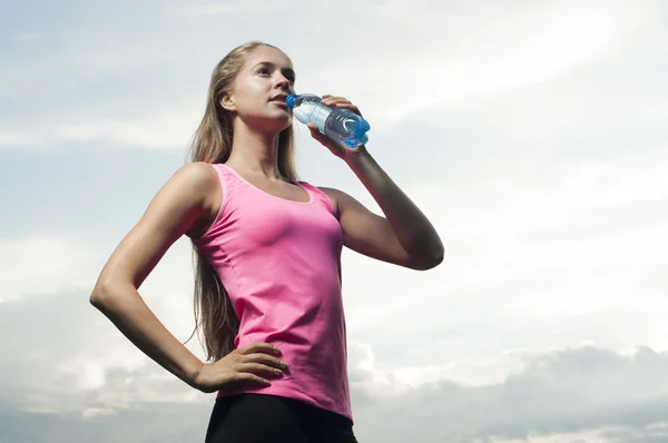 Sports female drinks water against the sky