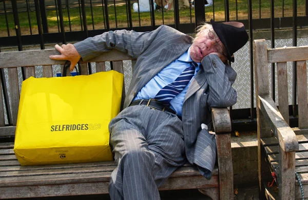 Worn out, old man asleep in street bench in London with yellow Selfridge\'s shopping bag