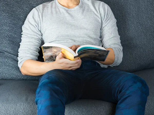 Man reading book on sofa; chilling and reading concept