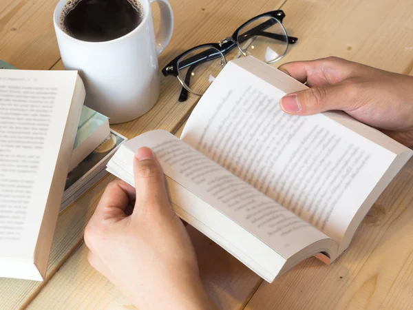 Man hand reading book, blurred text content, with coffee and eye