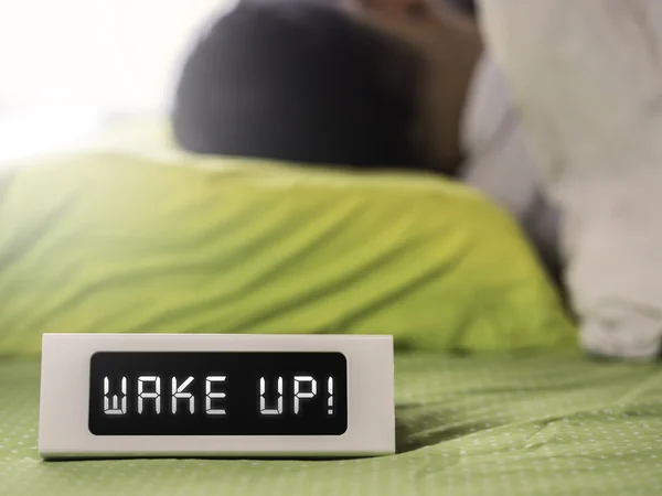 Wake up on digital clock with man sleeping in the background