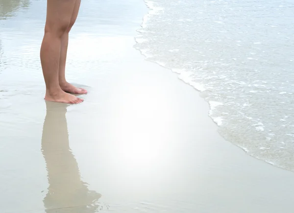 Person's leg standing on beach with tidal waves