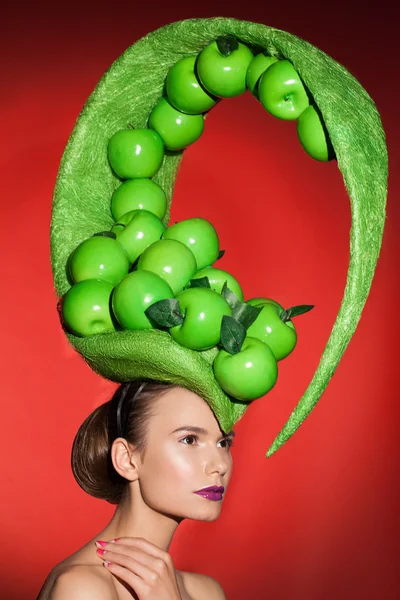 Magnificent green hat with green apples on head of young pretty model.