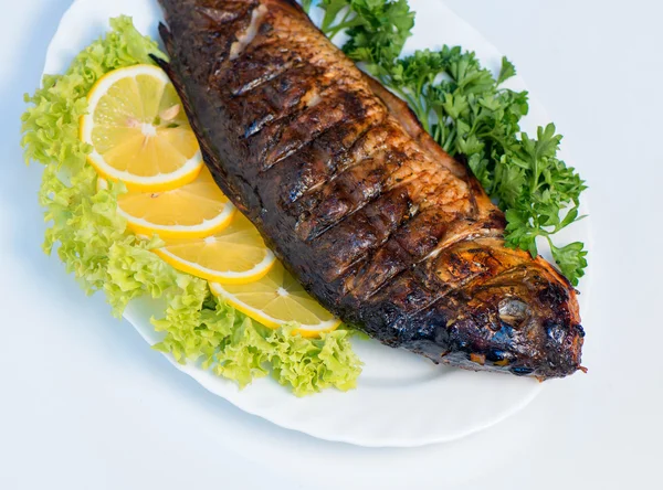 Fish cooked on fire on a white plate with lettuce leaves and par