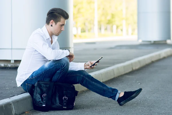 Handsome young man using smartphone while sitting near road