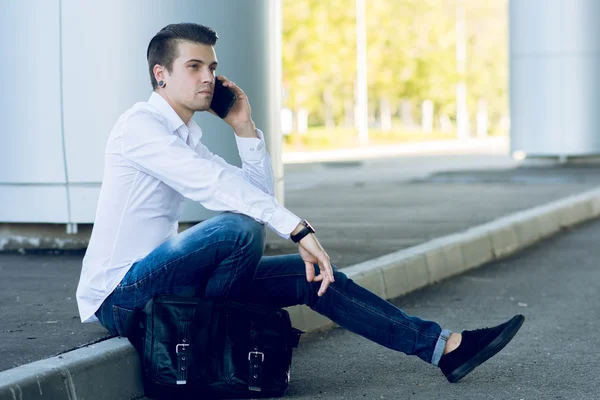 Handsome young man talking smartphone while sitting near road