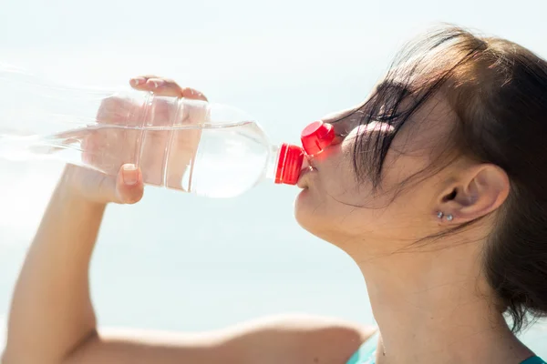 Fitness woman drinking water after running at beach