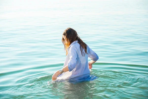 Woman on sea get into the water in wet shirt