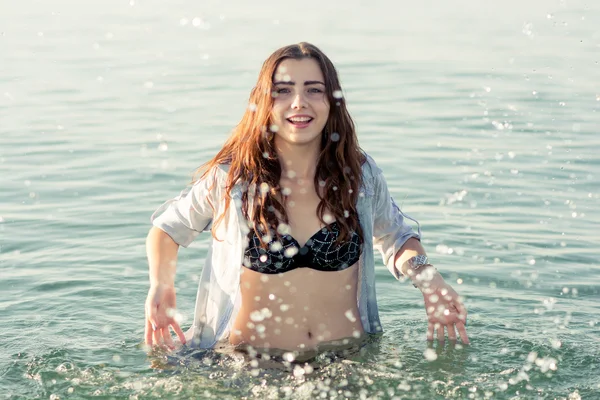 Beautiful young girl splashing the water in the sea